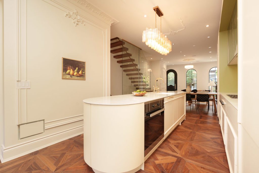 Modern kitchen featuring elegant hardwood flooring installed by Oakland Hardwood Flooring. The kitchen includes a stylish marble island with bar stools, sleek cabinetry, a vibrant green backsplash, and a statement chandelier, showcasing the seamless integration of premium hardwood flooring with contemporary kitchen design.